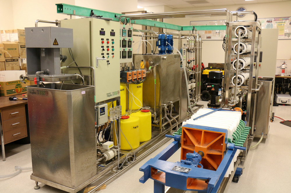 A sophisticated industrial water treatment unit featuring metal tanks, filtration piping, and monitoring gauges, designed to fit within a mobile trailer for field deployment.