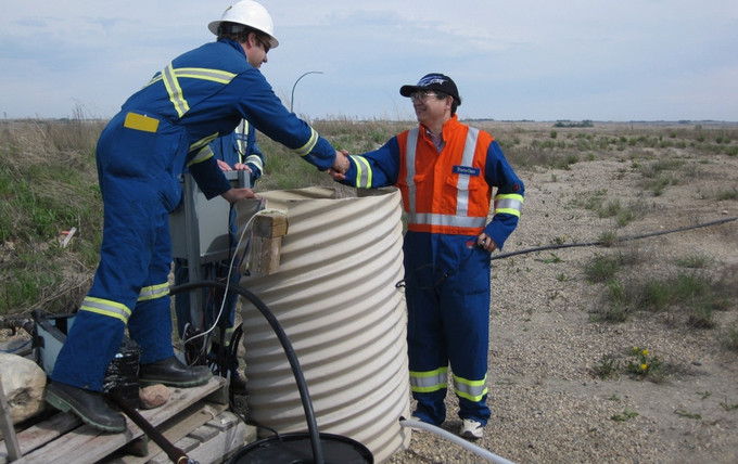two men working on equipment on the back of a red pickup truck in a snowy field setting.