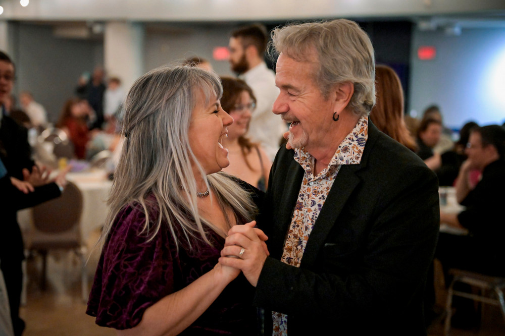 Two people laugh and dance together, holding hands on a busy dance floor.