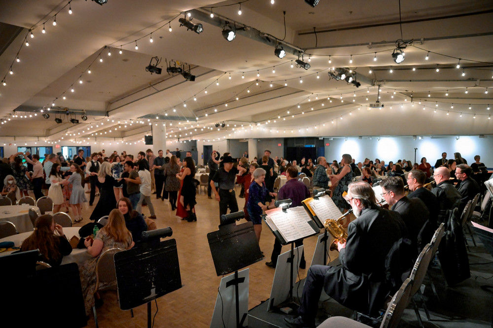 A wide view of a large crowd dancing under string lights while a live big band performs on stage.
