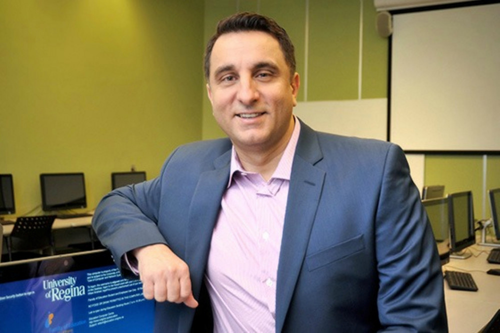 Dr. Alec Couros leans casually against a computer displaying the University of Regina website in a campus computer lab