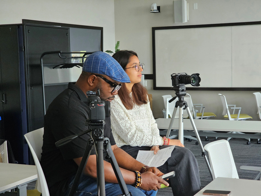 Three EDI Digital Resource Hub team members stand outdoors wearing University of Regina shirts, with trees and water visible in the background.