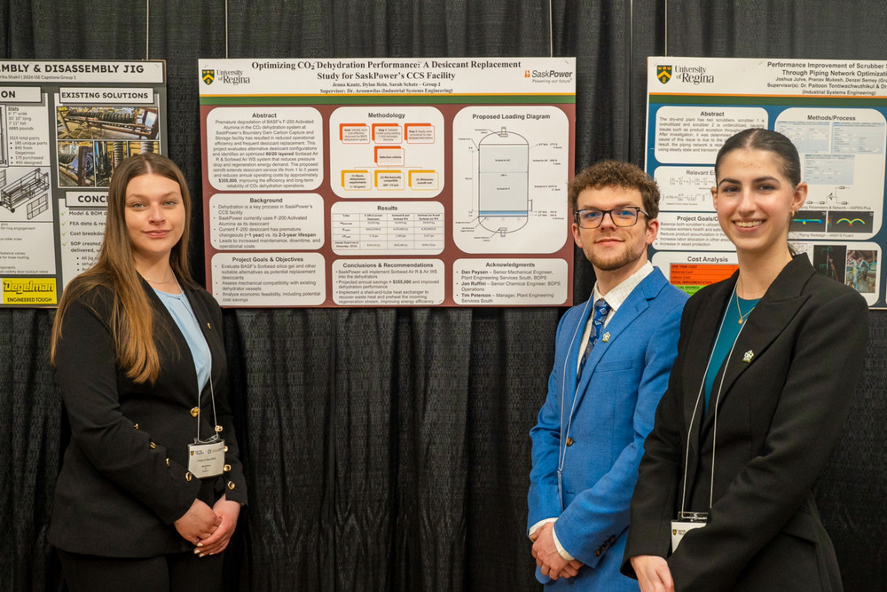 Three people smiling and dressed professionally standing in front of a poster