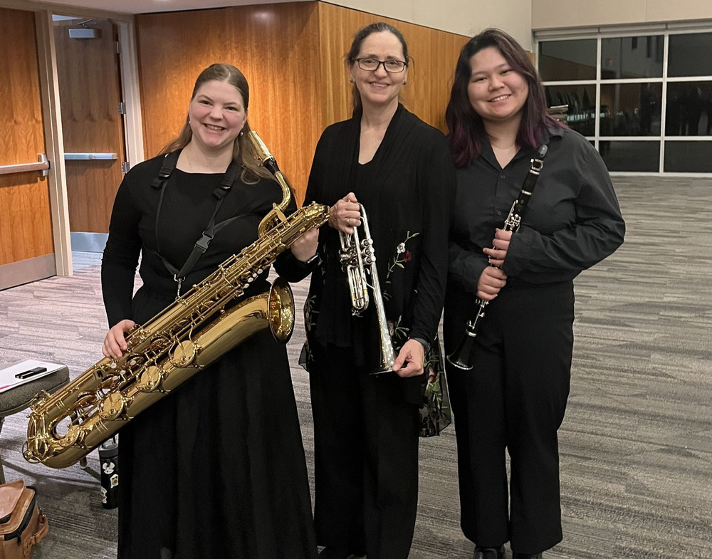 Three students standing in front of a MusicFest Canada banner, holding their instruments