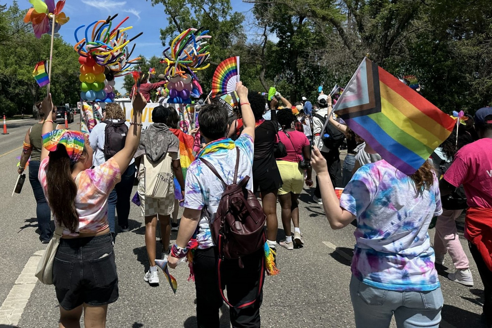 Parade participants walking closely together, some wearing rainbow bandanas and using a bubble gun, with the float moving ahead.