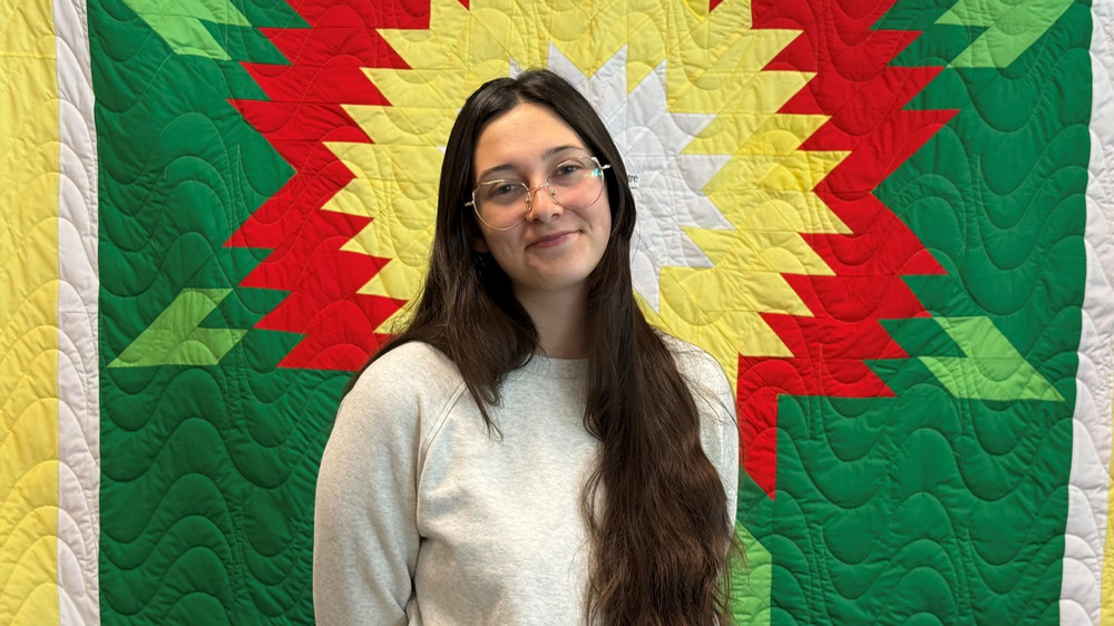 A young woman stands in front of a colourful blanket
