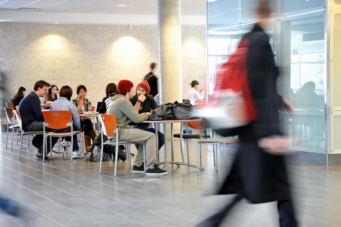 Students collaborate at tables in a bright University of Regina campus atrium while a student walks past in the foreground.