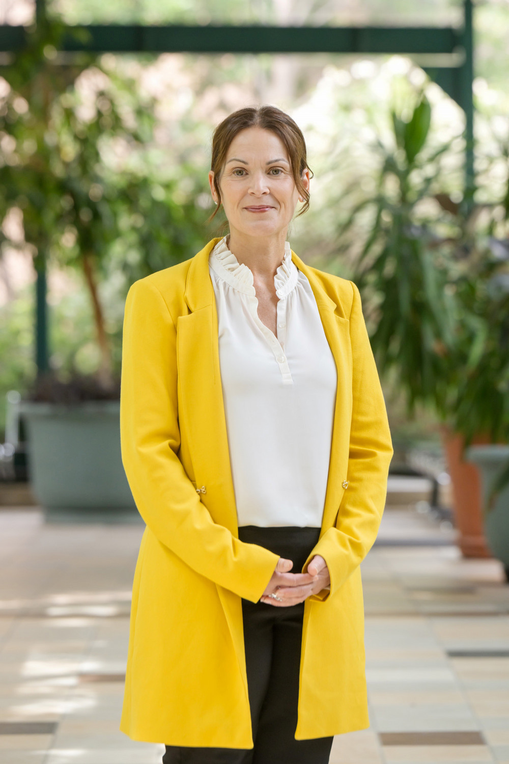 A woman in a yellow sweater poses in a light-filled atrium. 
