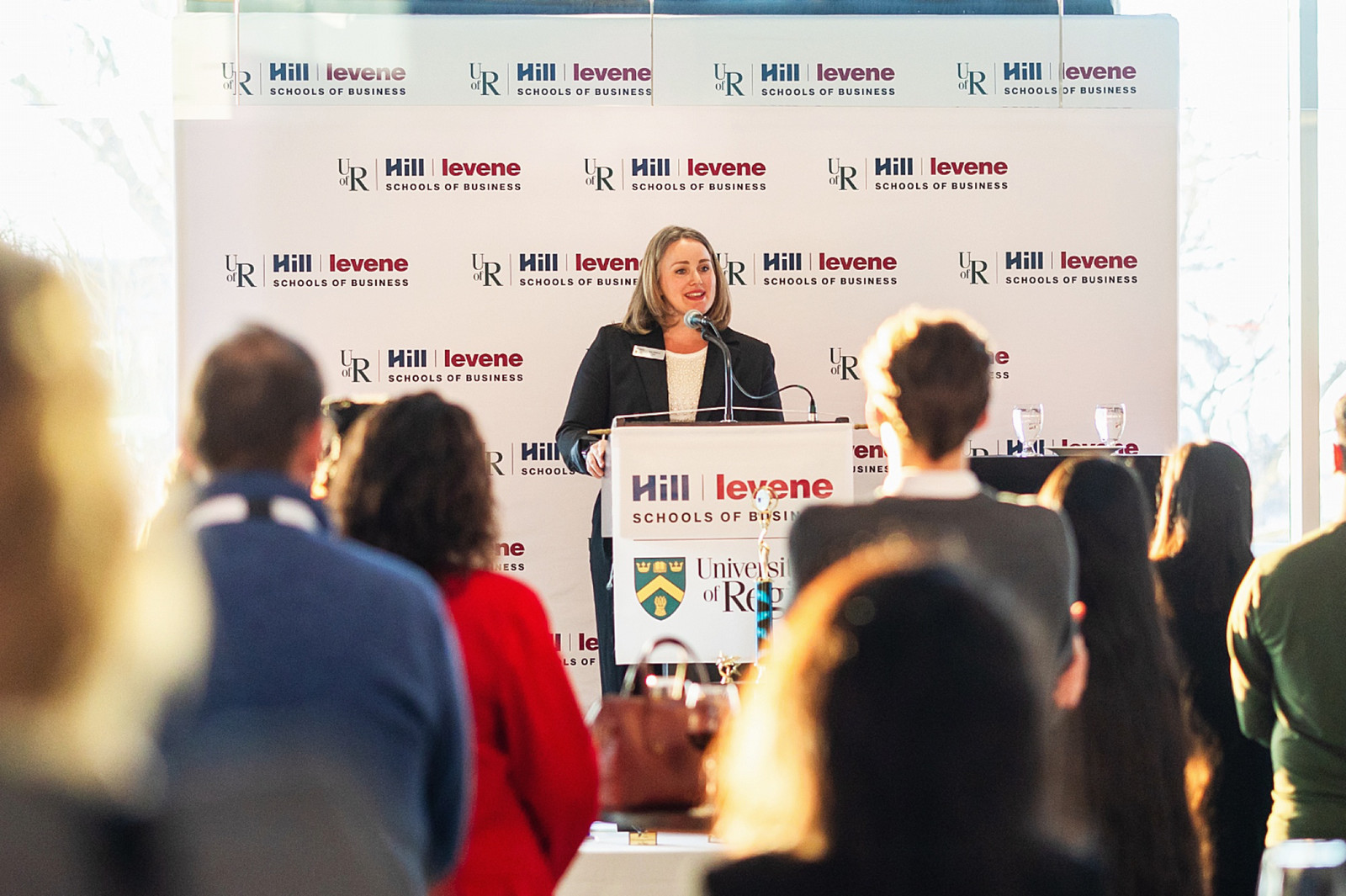 Dean Erin Oldford addresses an audience from a podium featuring the Hill Levene School of Business logo