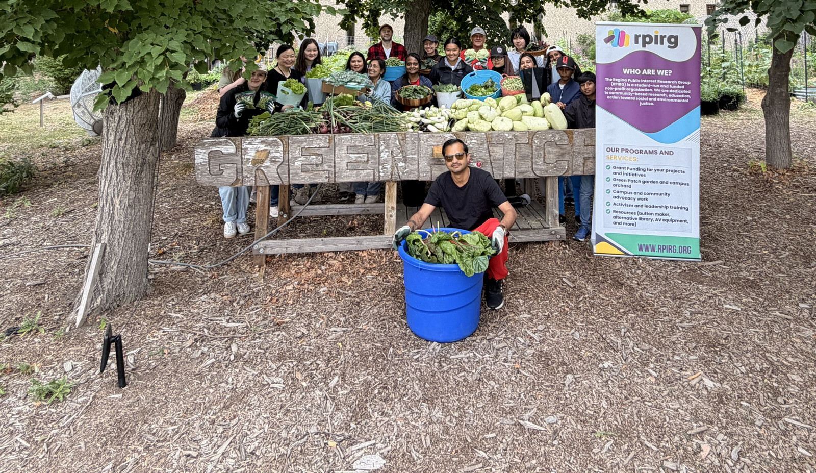 Table with vegetables surrounded by people.