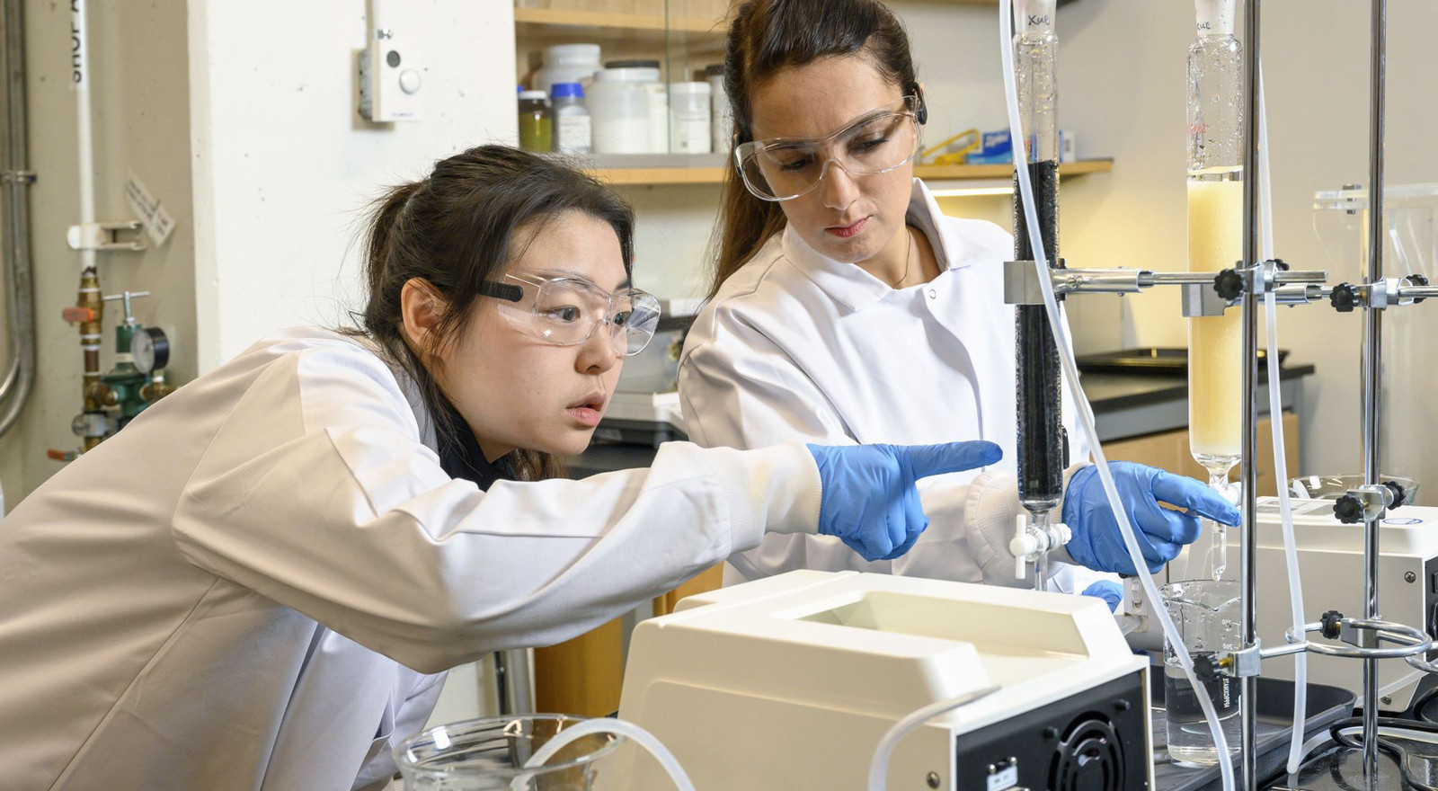 Two women monitor equipment as they conduct an experiment in a laboratory