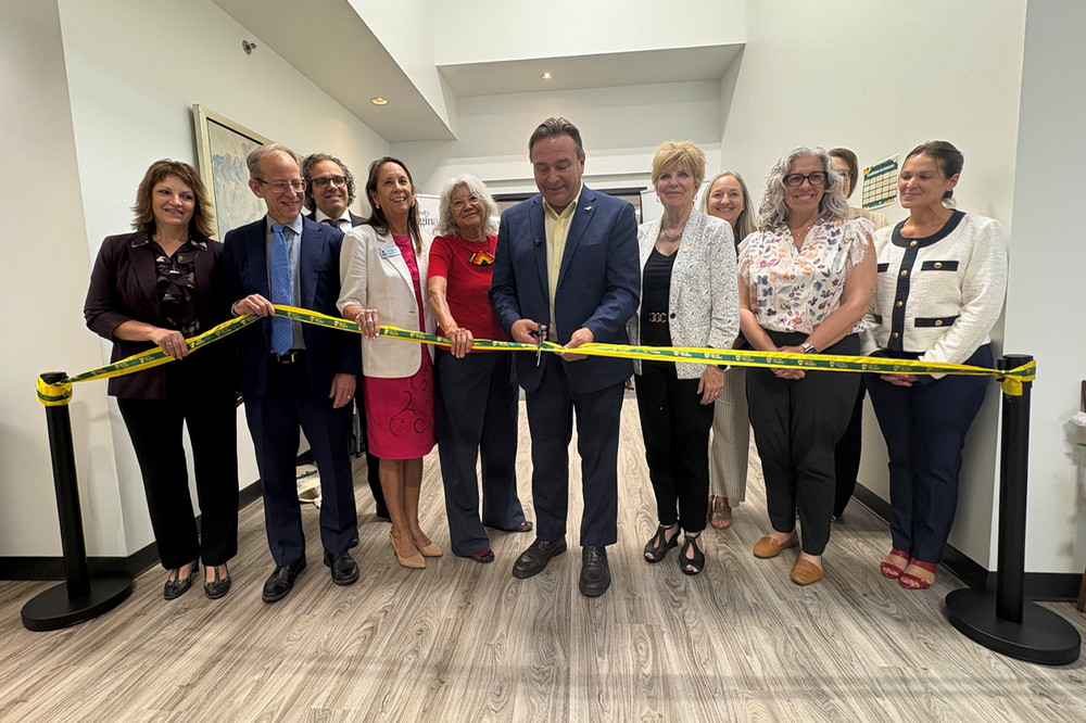  A man stands with a group of people behind a ribbon which he is cutting. 