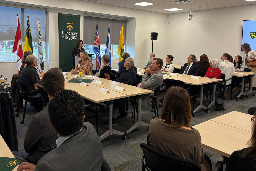 A group of people assembled in a classroom where a woman is talking behind a podium. 