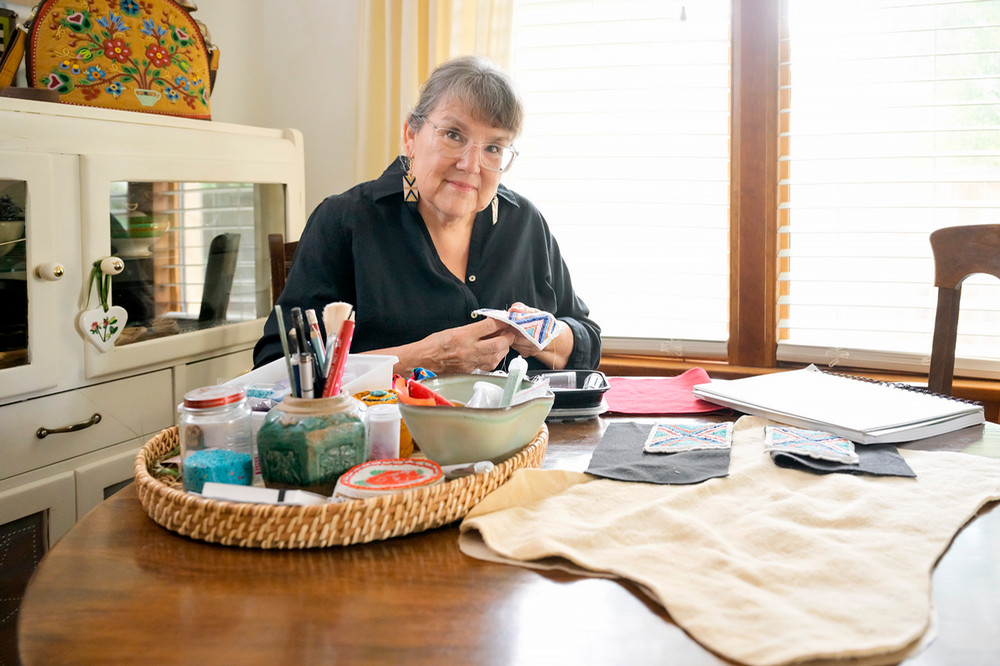 A woman sits at a table with art materials spread on the table