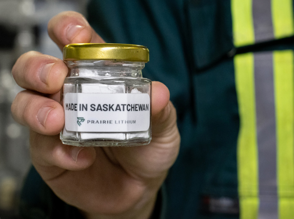 Close-up of a worker's hand holding a glass jar of extracted white lithium labelled “Made in Saskatchewan” and “Prairie Lithium”