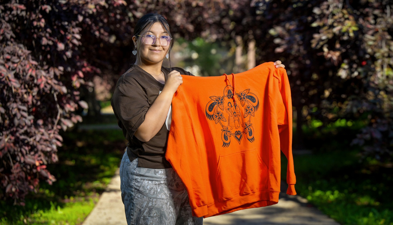 A person holding an orange hoodie featuring the artwork.