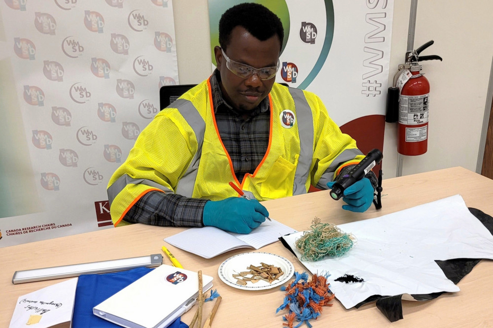  A student in a lab writes in a notebook while holding a handheld scanner, with twine and plastic film on the table in front of them.