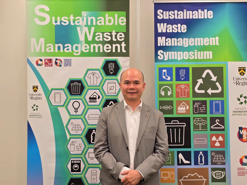 A person standing in front of two Sustainable Waste Management symposium banners and smiling.