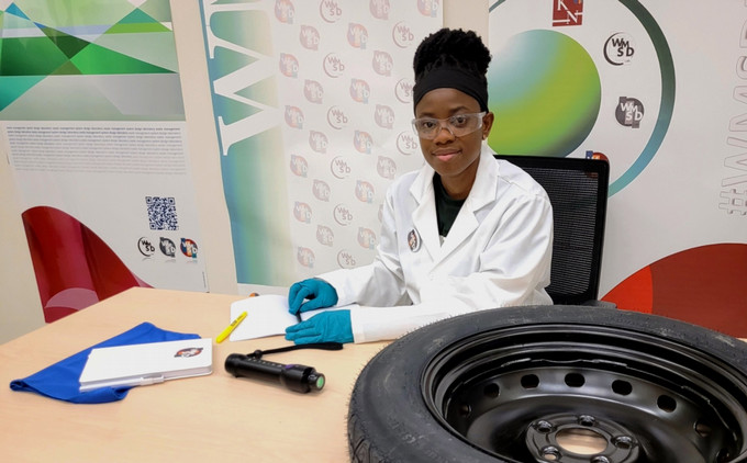 Student wearing a lab coat and safety glasses, sits with a scrap tire and a scanner