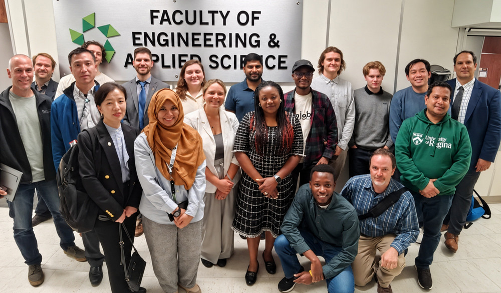 About 20 people stand together in front of a Faculty of Engineering and Applied Science sign.