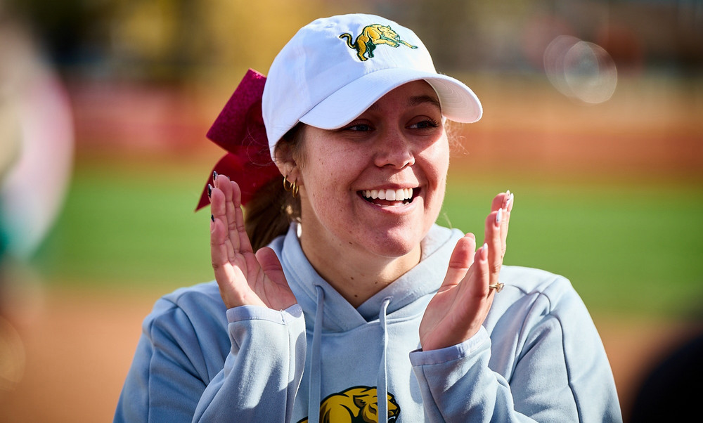 A close up of a woman in a baseball cap applauding. 