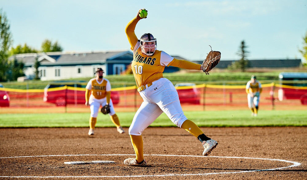 A young woman prepares to launch a softball pitch while on the pitcher’s mound. 