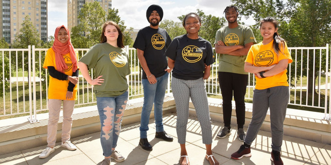 six smiling students standing outside on a sunny day