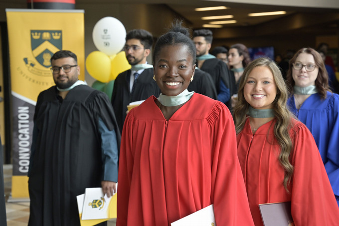 A group of graduates in black gowns smile and hold their degree certificates at a convocation ceremony.