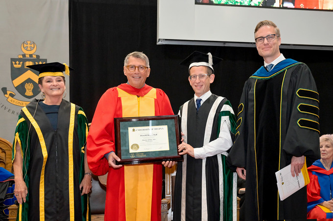 Four people standing and smiling and one person holding a diploma