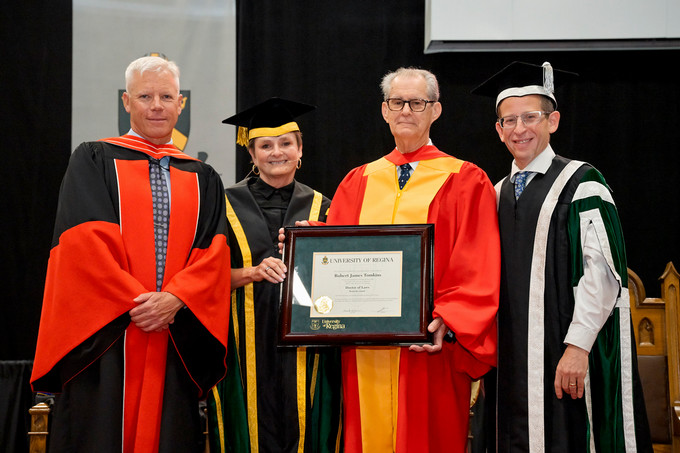 Four people standing and smiling and one person holding a diploma