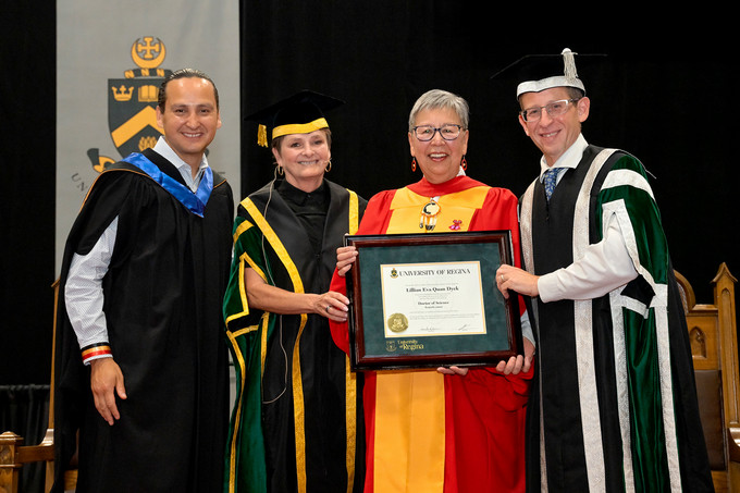 Four people standing and smiling and one person holding a diploma
