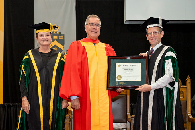 Four people standing and smiling and one person holding a diploma