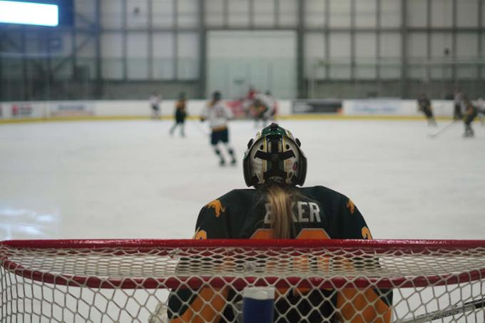 A hockey game as viewed from behind the goalie at one end of the rink.