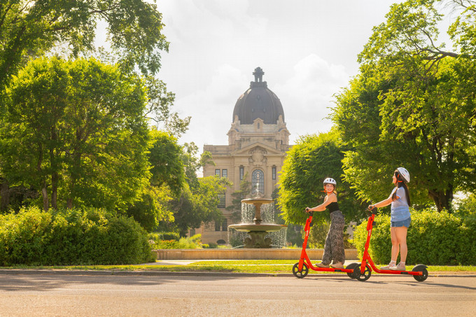 Two girls on scooters in the park.