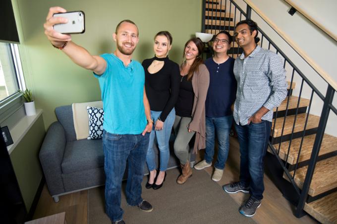 Students standing by stairway taking selfies.