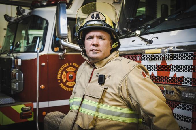 A fireman poses for a photo inside a firehouse, wearing all of his safety gear.