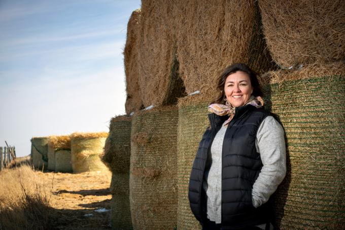 Cynthia Beck outdoors on farm leaning against stack of round bales