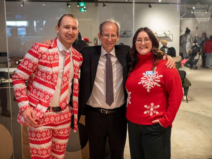 Two students in Christmas suits pose with the university president